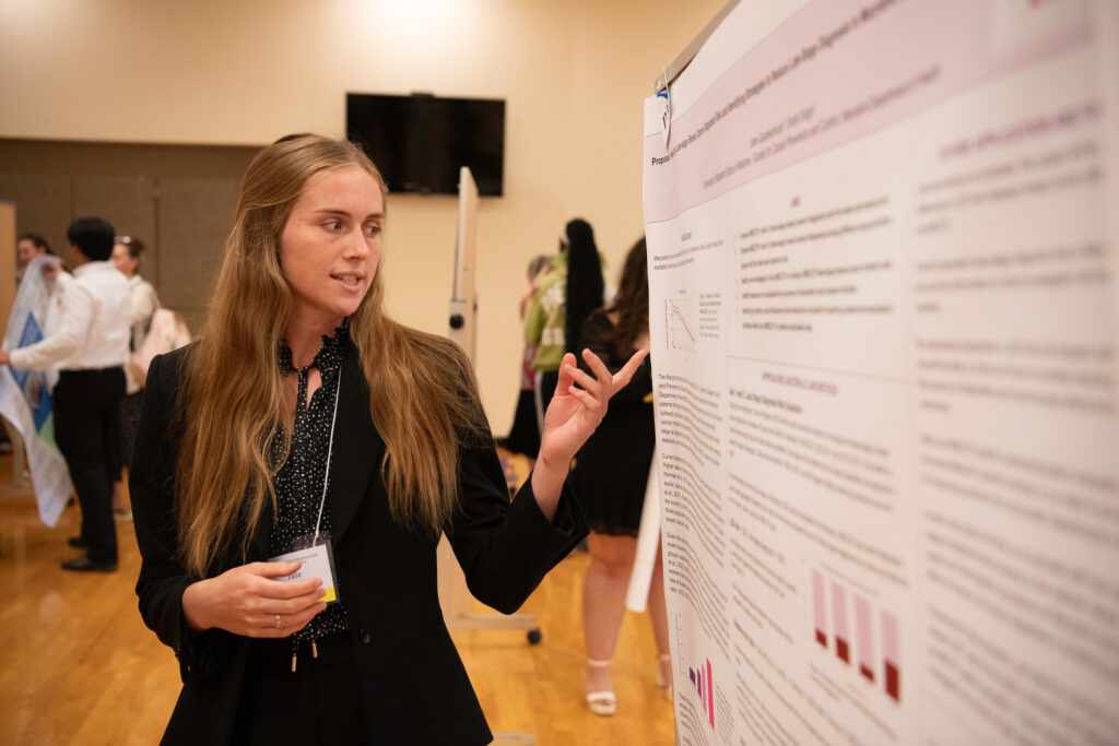 Female student points to research presentation poster.